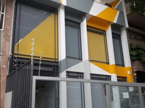 Texto Alternativo (10 palavras): Fachada comercial moderna com pintura geométrica amarela cinza e branca